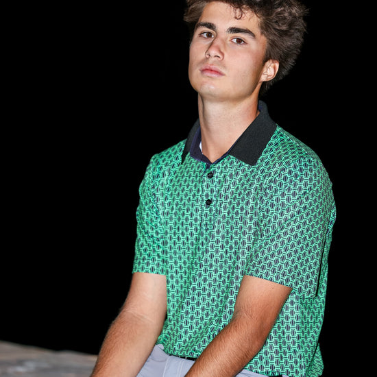 Man wearing a green patterned polo shirt sitting on a dark background