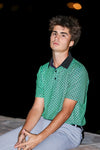 Man wearing a green patterned polo shirt sitting on a dark background