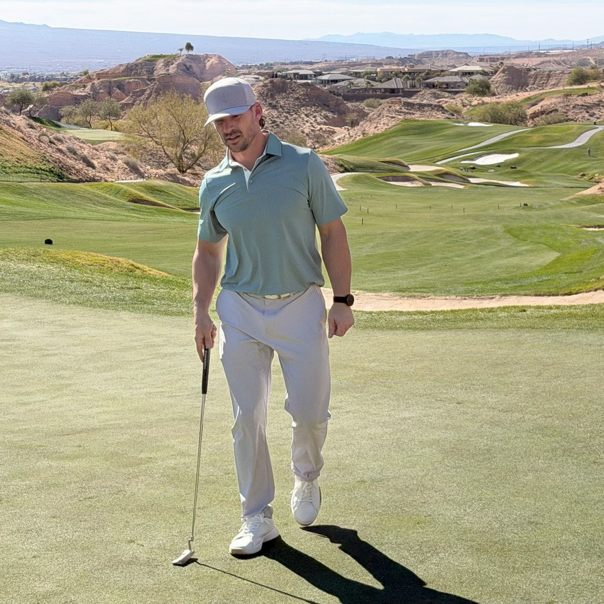 Man on a golf course holding a golf club with a scenic background