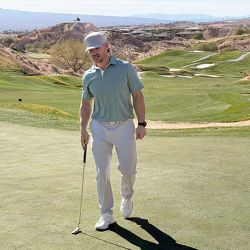 Man on a golf course holding a golf club with a scenic background