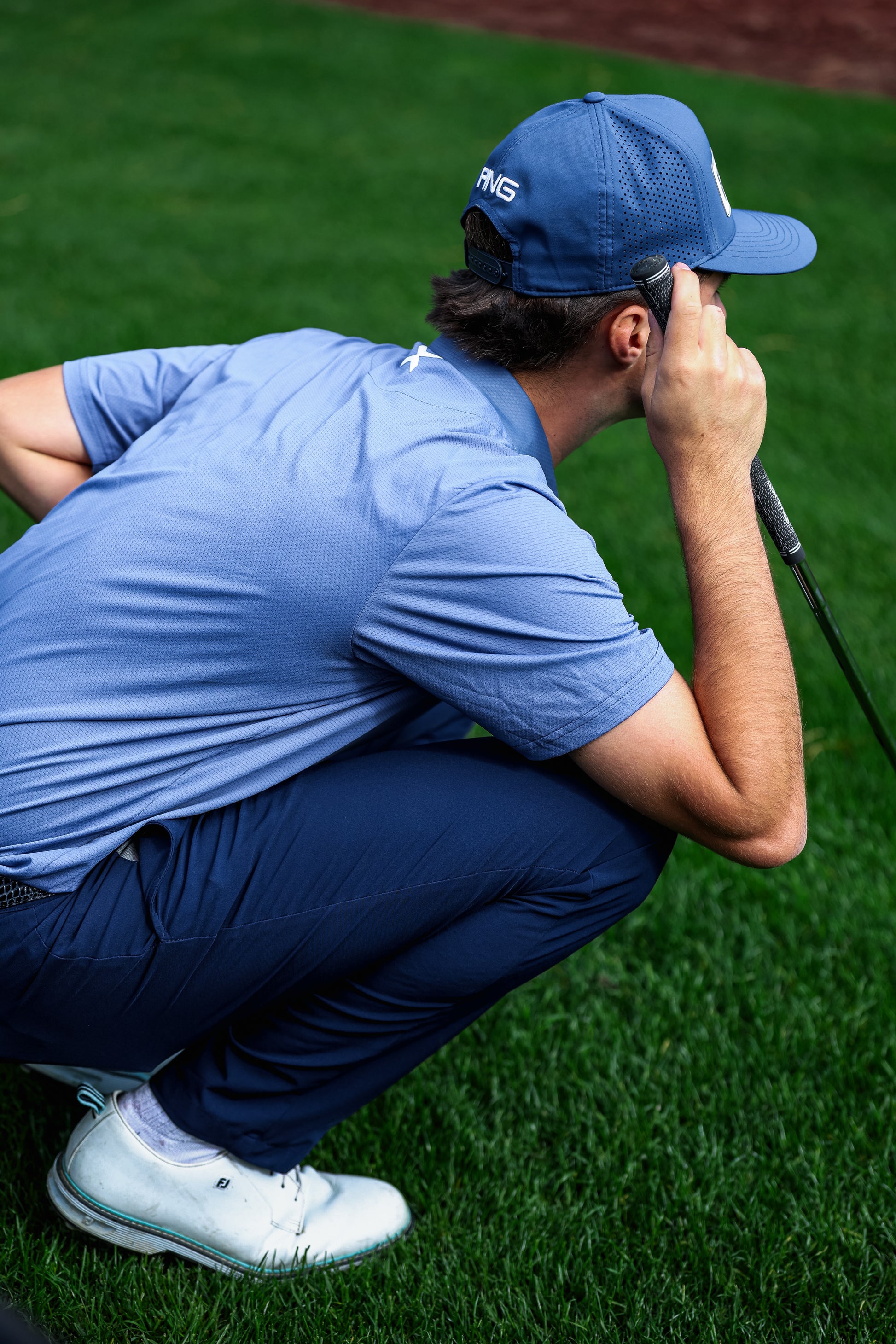 Golfer in blue outfit adjusting cap on a green golf course