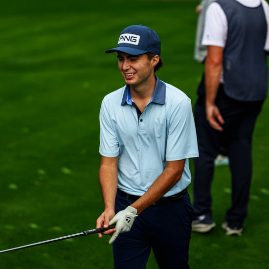Golfer on a golf course holding a club with another person in the background.
