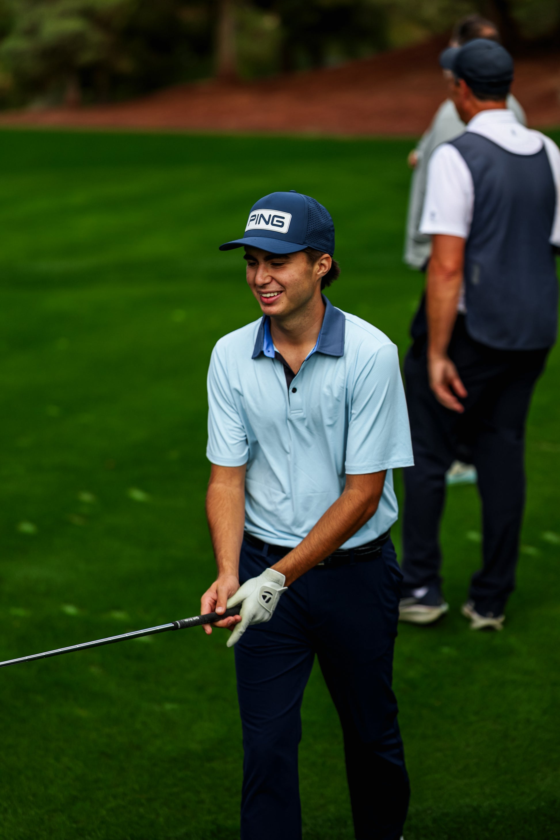 Golfer on a golf course holding a club with another person in the background.