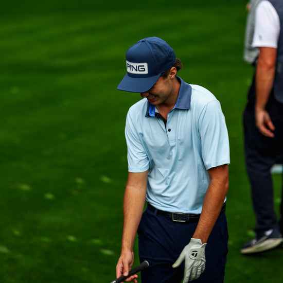 Man in light blue shirt and dark pants on a golf course, holding a golf club.