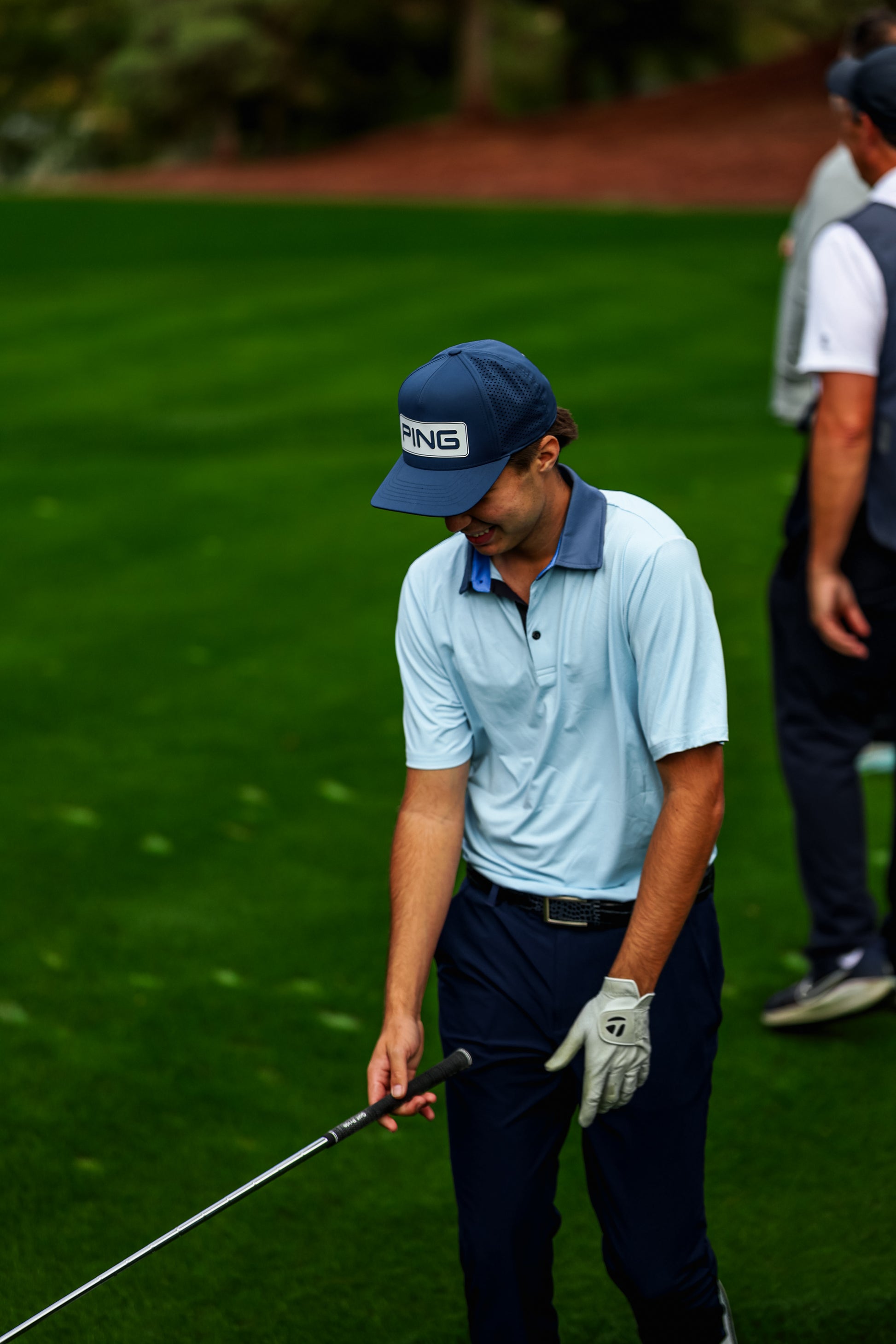Man in light blue shirt and dark pants on a golf course, holding a golf club.