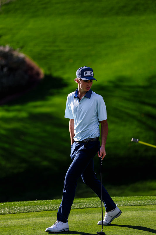 Golfer on a green golf course wearing a cap and white shirt.