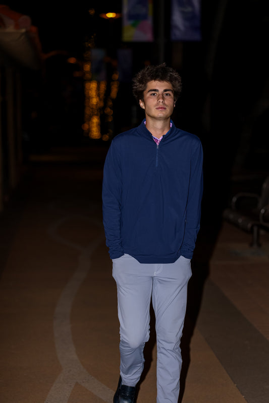Man wearing a blue jacket and light pants standing in a dimly lit indoor setting.